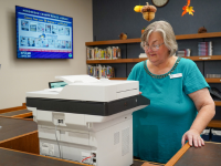 Lady standing in the library at a fax machine and pressing buttons