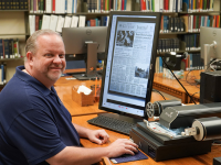 Adult sitting in front of a microfilm machine at the library