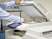 One hand holding up a printer lid while the other hand places a piece of paper down to copy