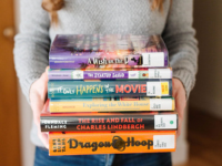 Woman holding a stack of six different books with the book binds all visible