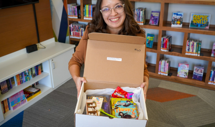 Female librarian smiling and holding a teen book box with various items