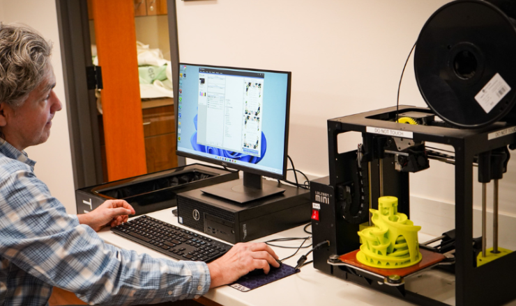Man working on a desktop computer next to a 3D printer